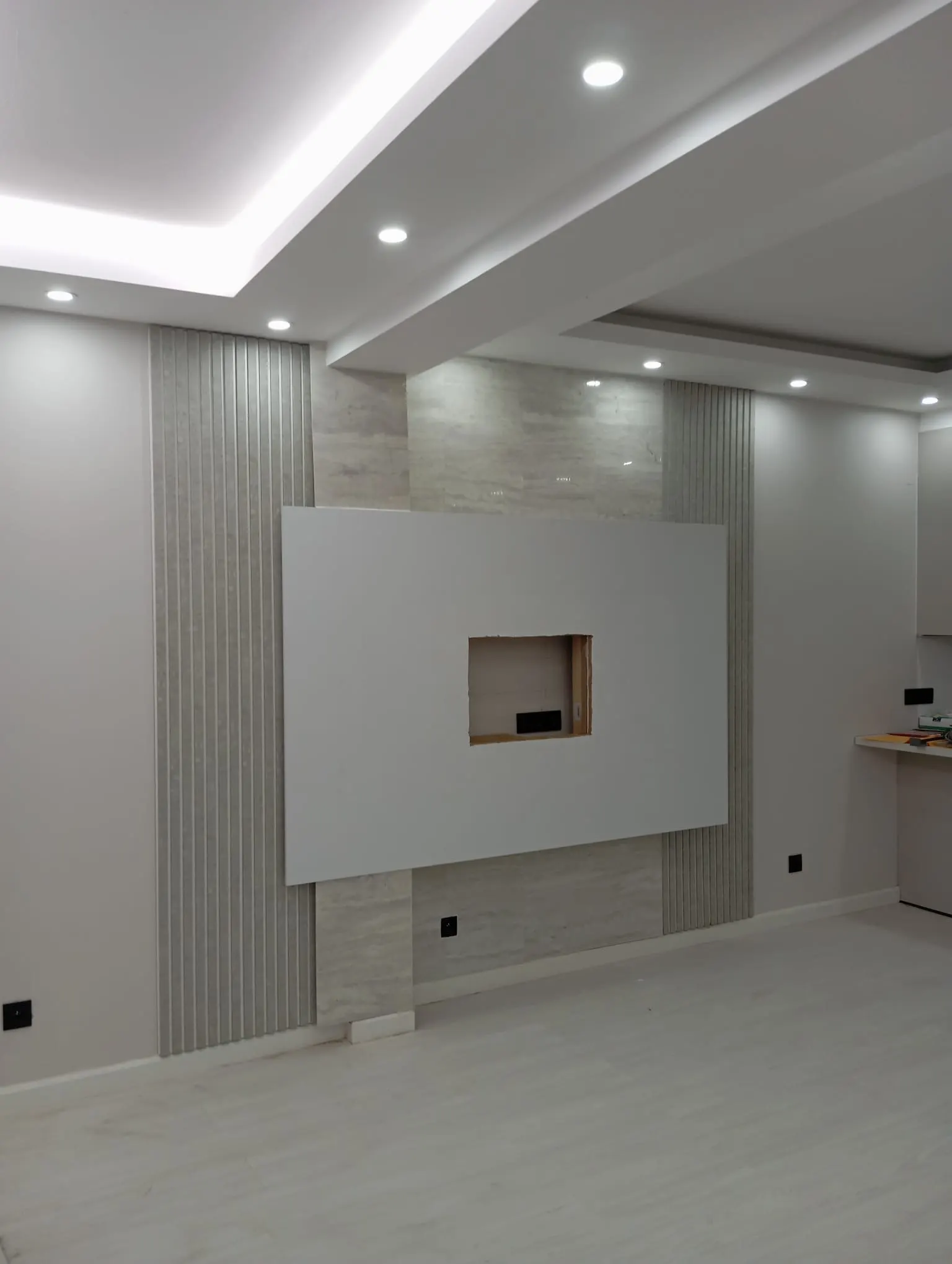 The same living-room wall finished: white TV wall with recess, slatted panels and ceiling spots