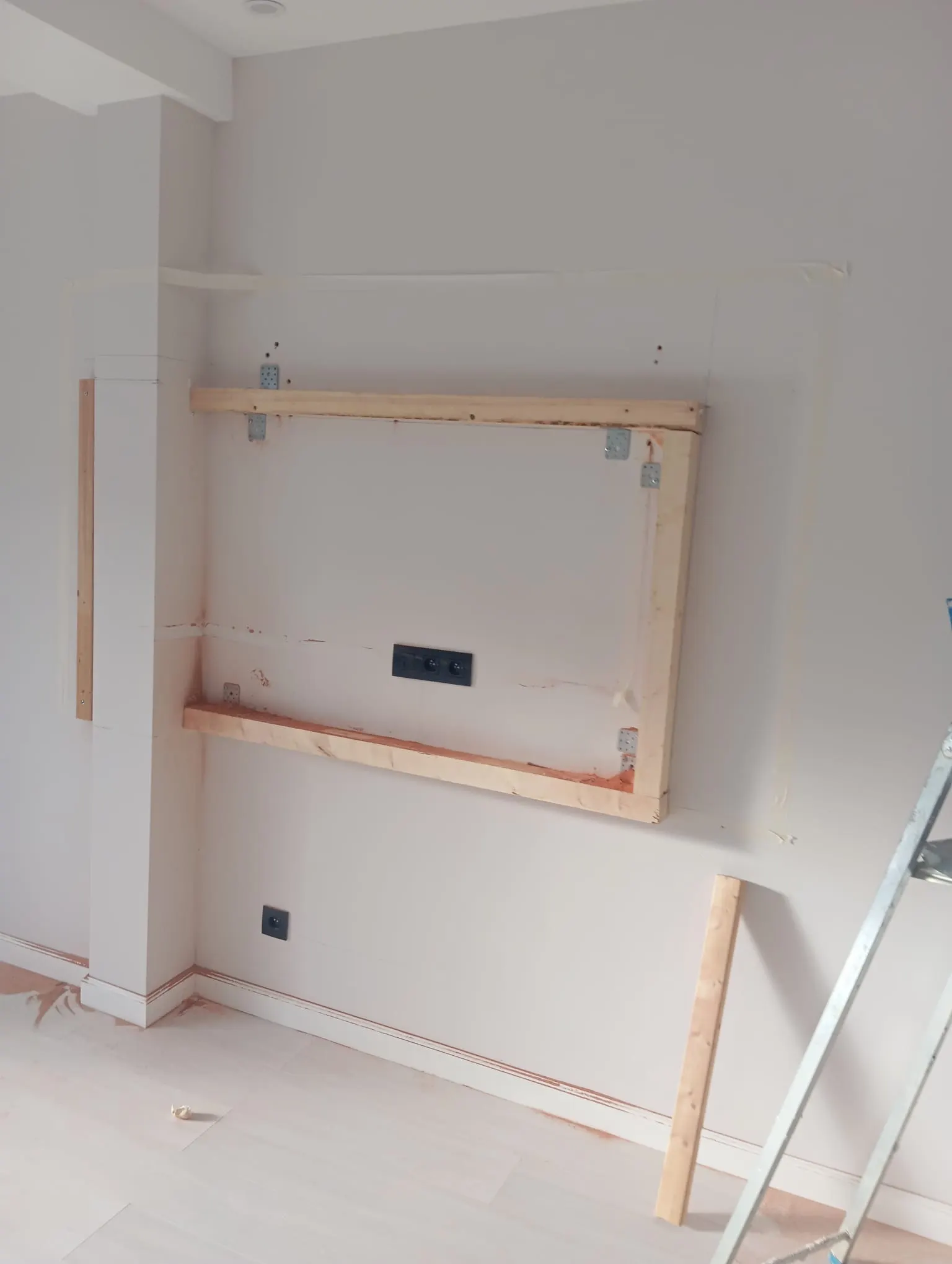 Living-room wall before finishing: timber frame for the TV wall against a bare, masked wall