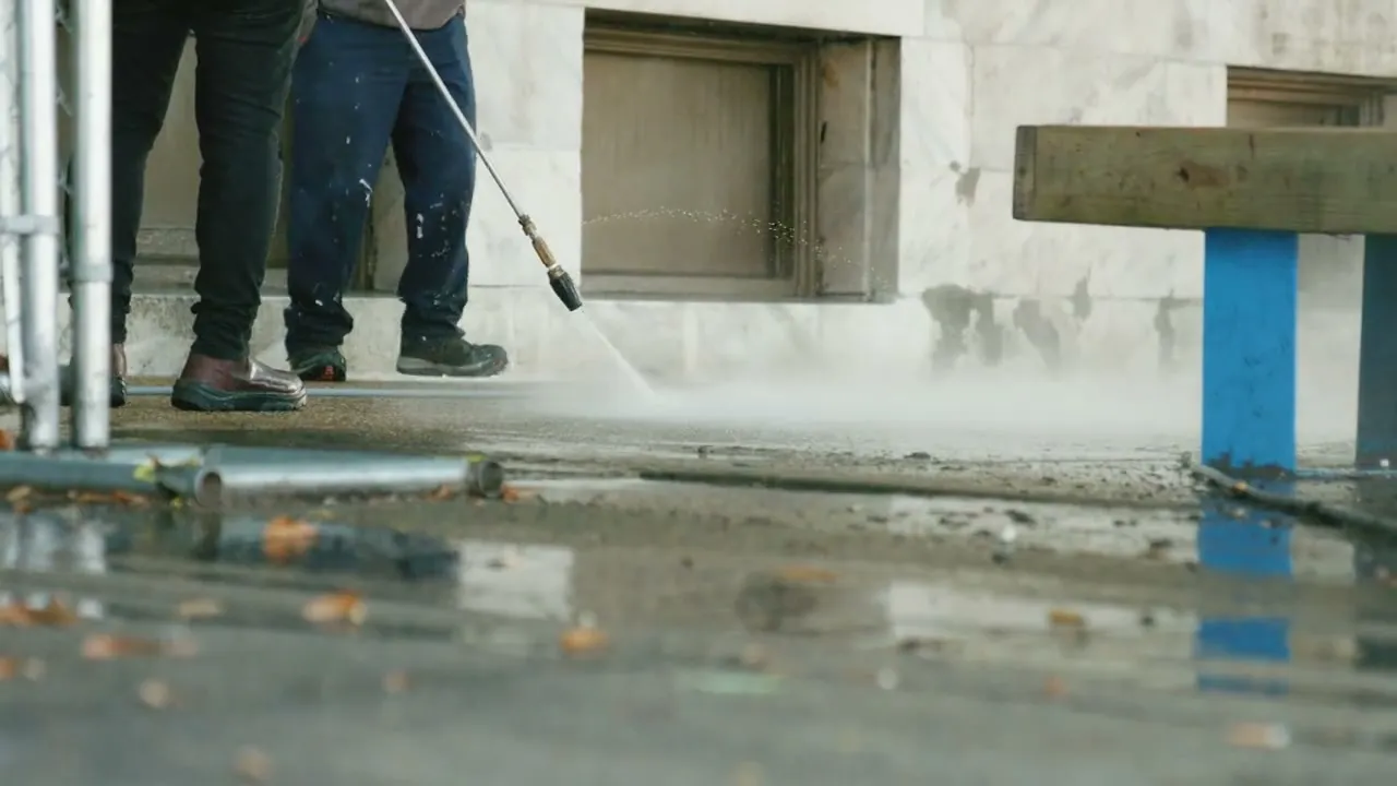 The high-pressure jet at work on a dirty outdoor floor alongside a facade