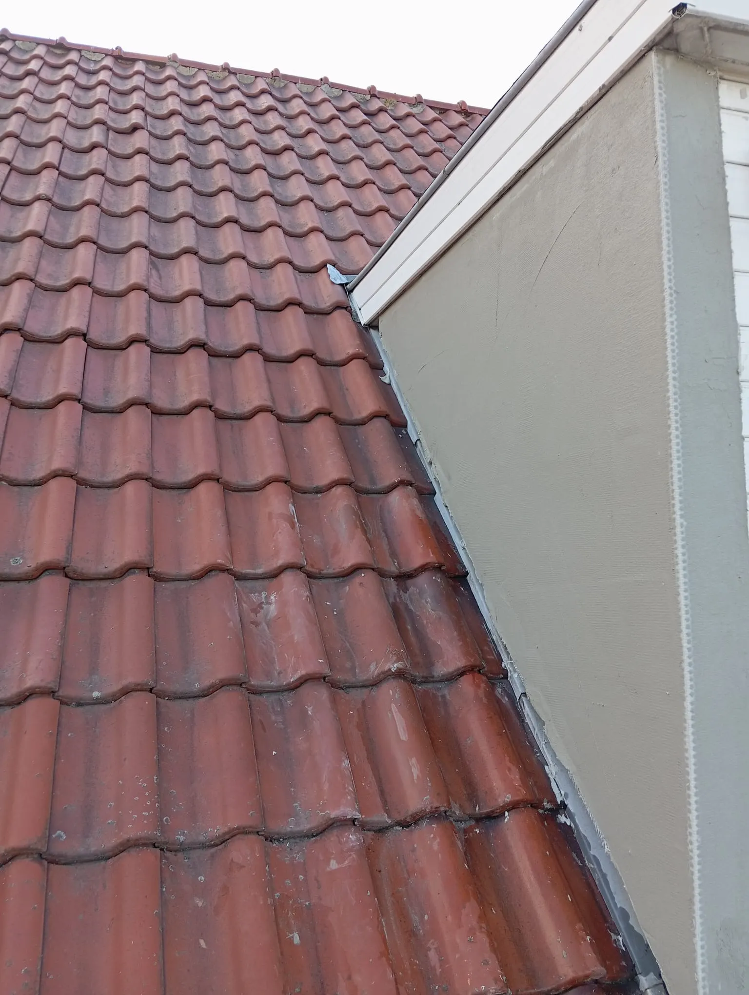 Toit en tuiles rouges raccordé à un mur latéral enduit, avec bavette en plomb et rive de gouttière