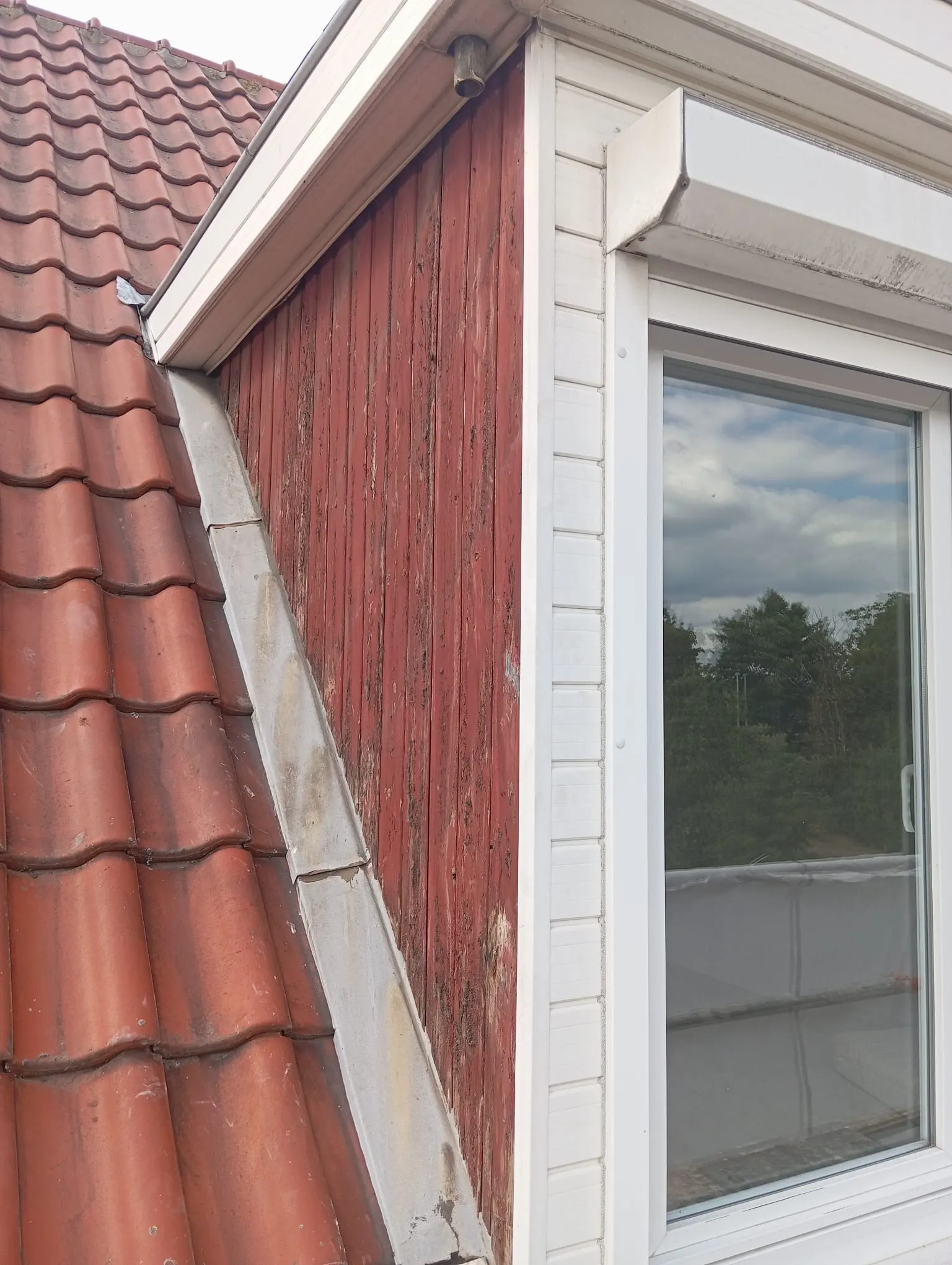 Lucarne au bardage bois rouge altéré, à côté d'un toit en tuiles, avant rénovation