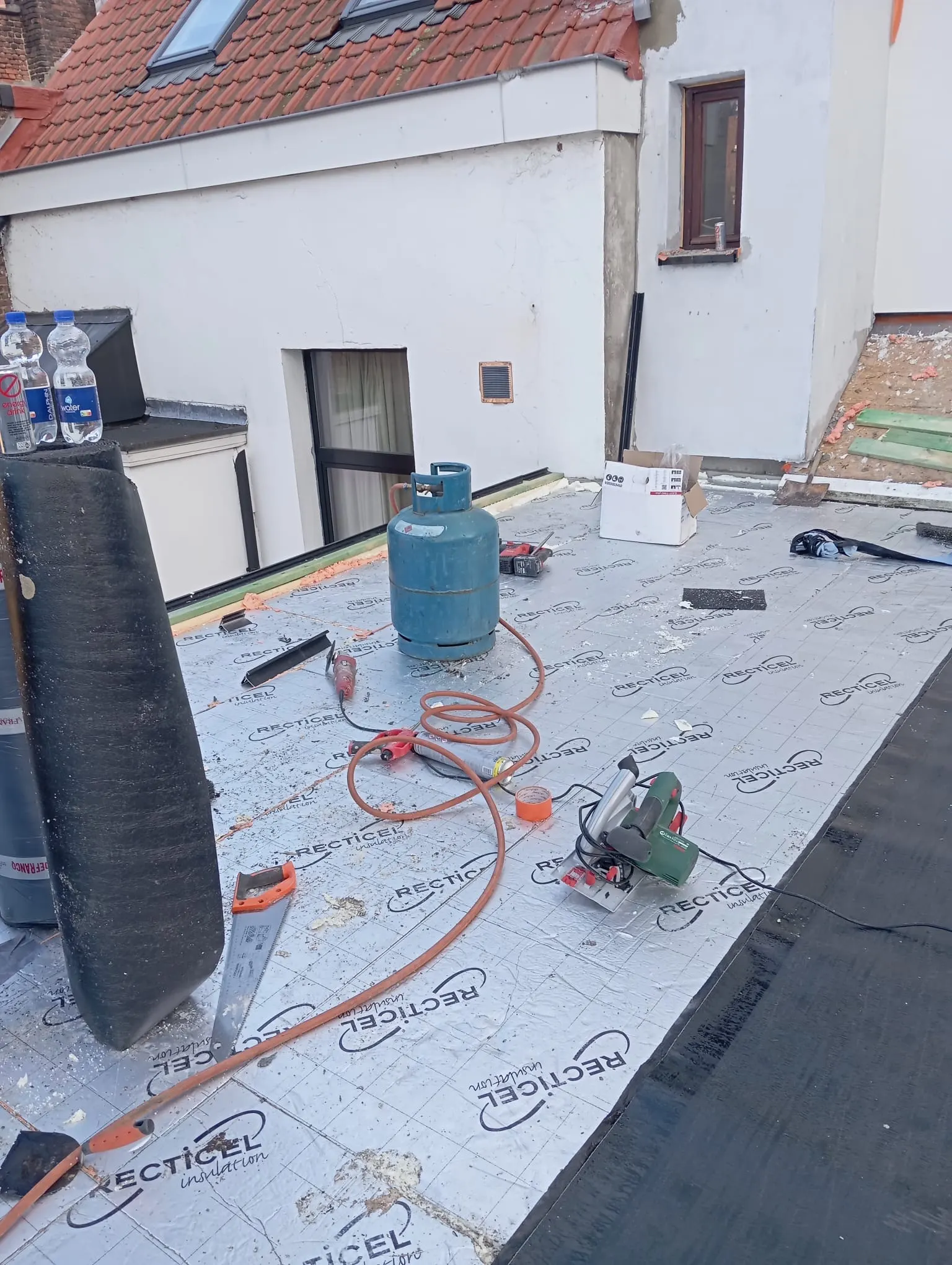 Toiture plate en cours : panneaux isolants posés, bonbonne de gaz, chalumeau et scie prêts