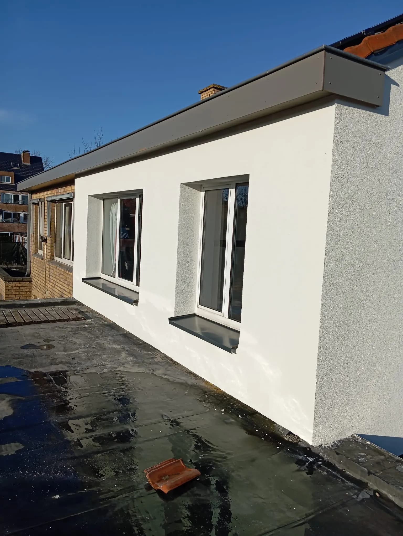Uitbouw met witte crepi-afwerking en twee ramen, afgewerkt dakrandprofiel