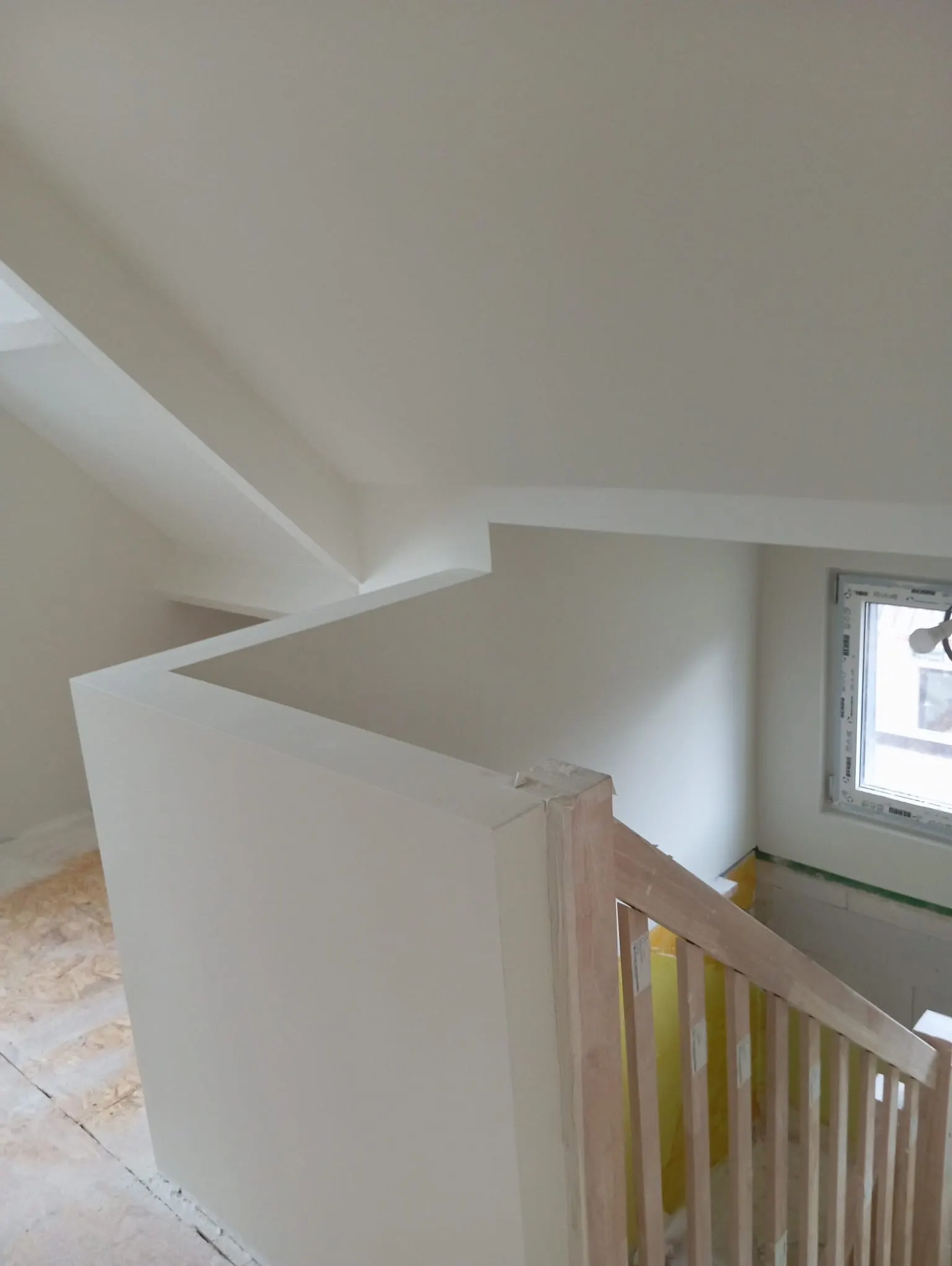 White-finished attic landing with a new wooden handrail and painted sloped walls