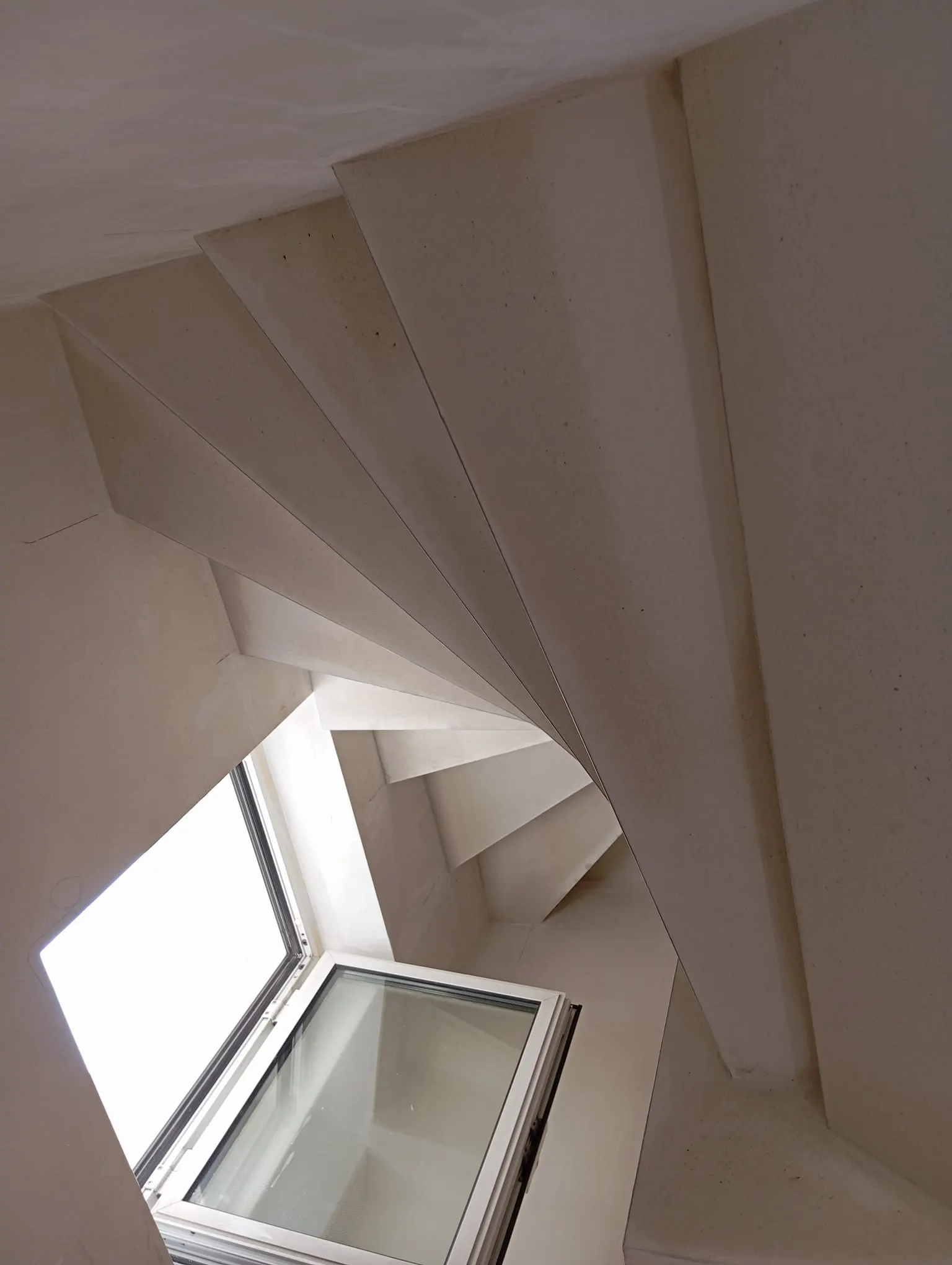 White-painted staircase seen from below, with a roof window and smooth wall and ceiling finish