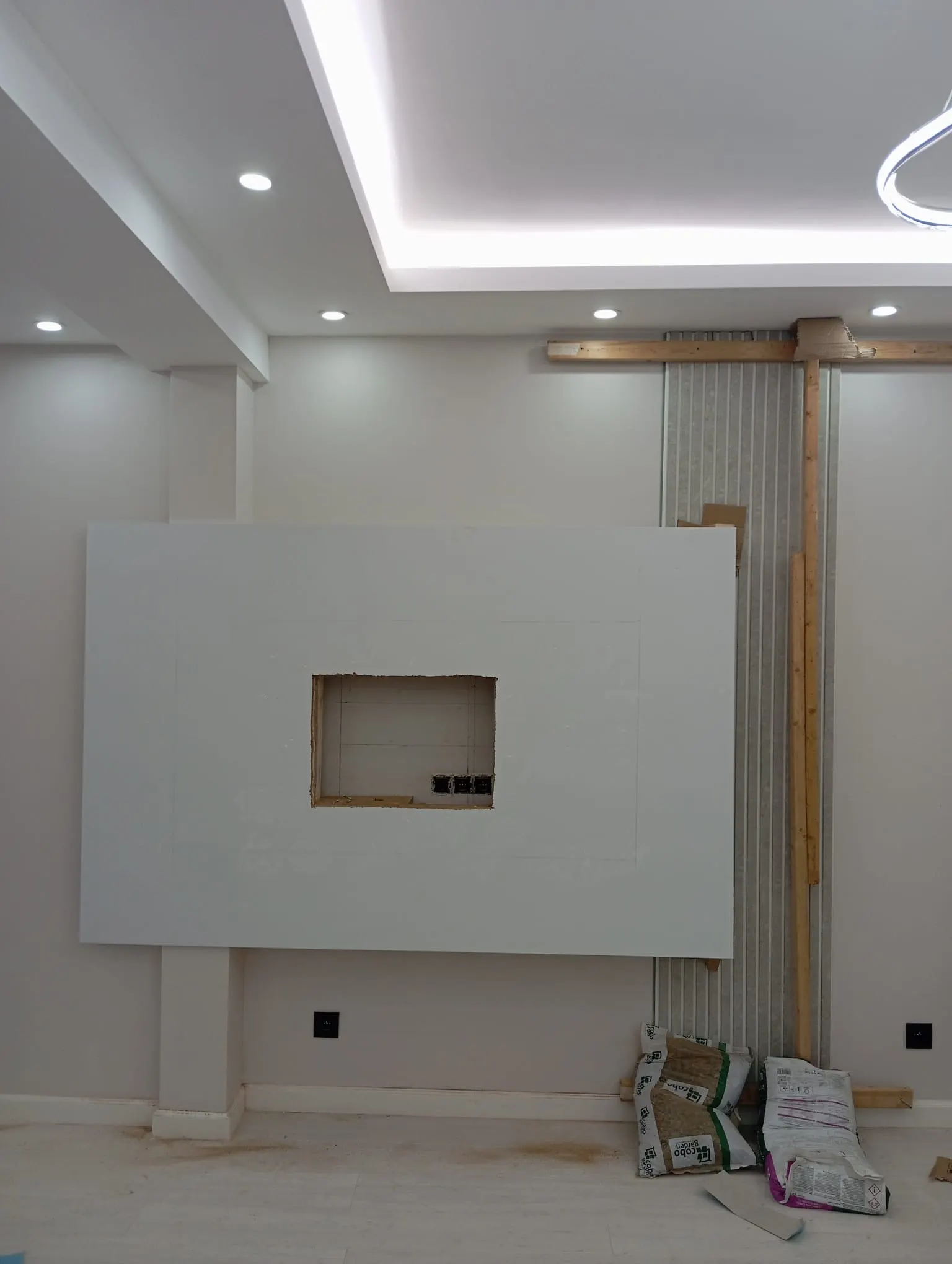 The same TV wall midway: plasterboard fitted with the recess left open, slatted panel half in place