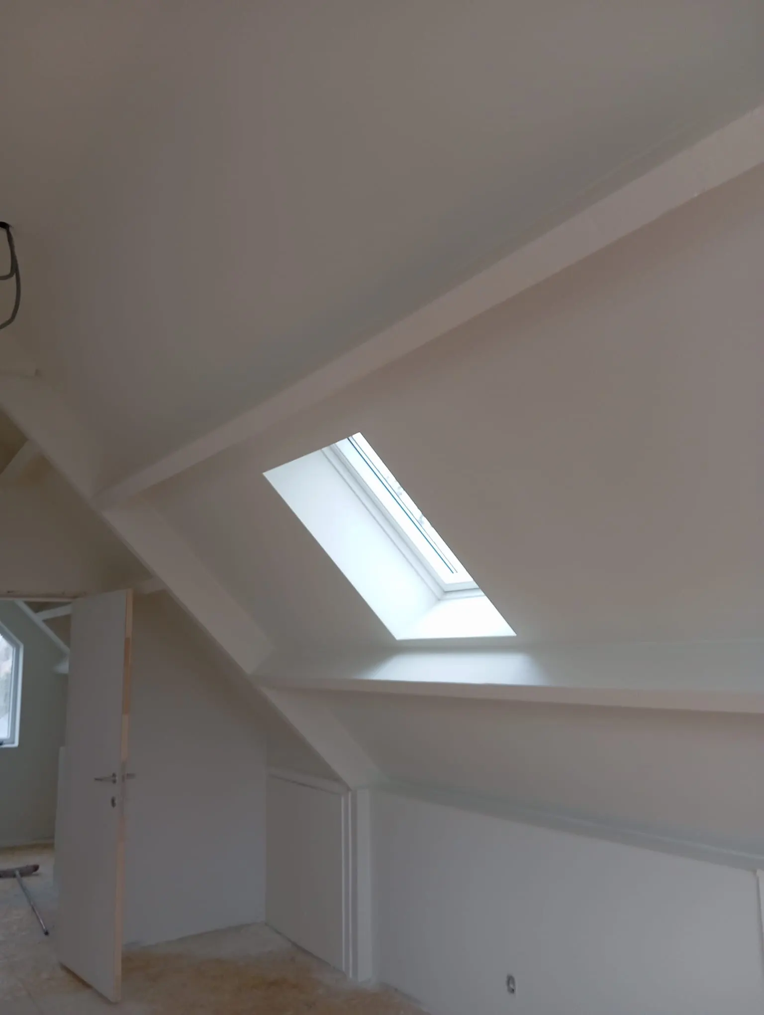 White-finished attic room with a roof window and neatly painted beams