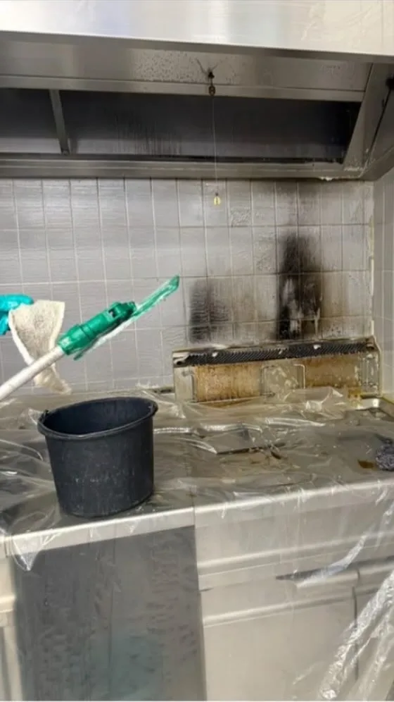 Professionele keuken voor de reiniging: aangekoekt vet op de grill, roetvlekken op de tegels en afdekfolie op het werkblad