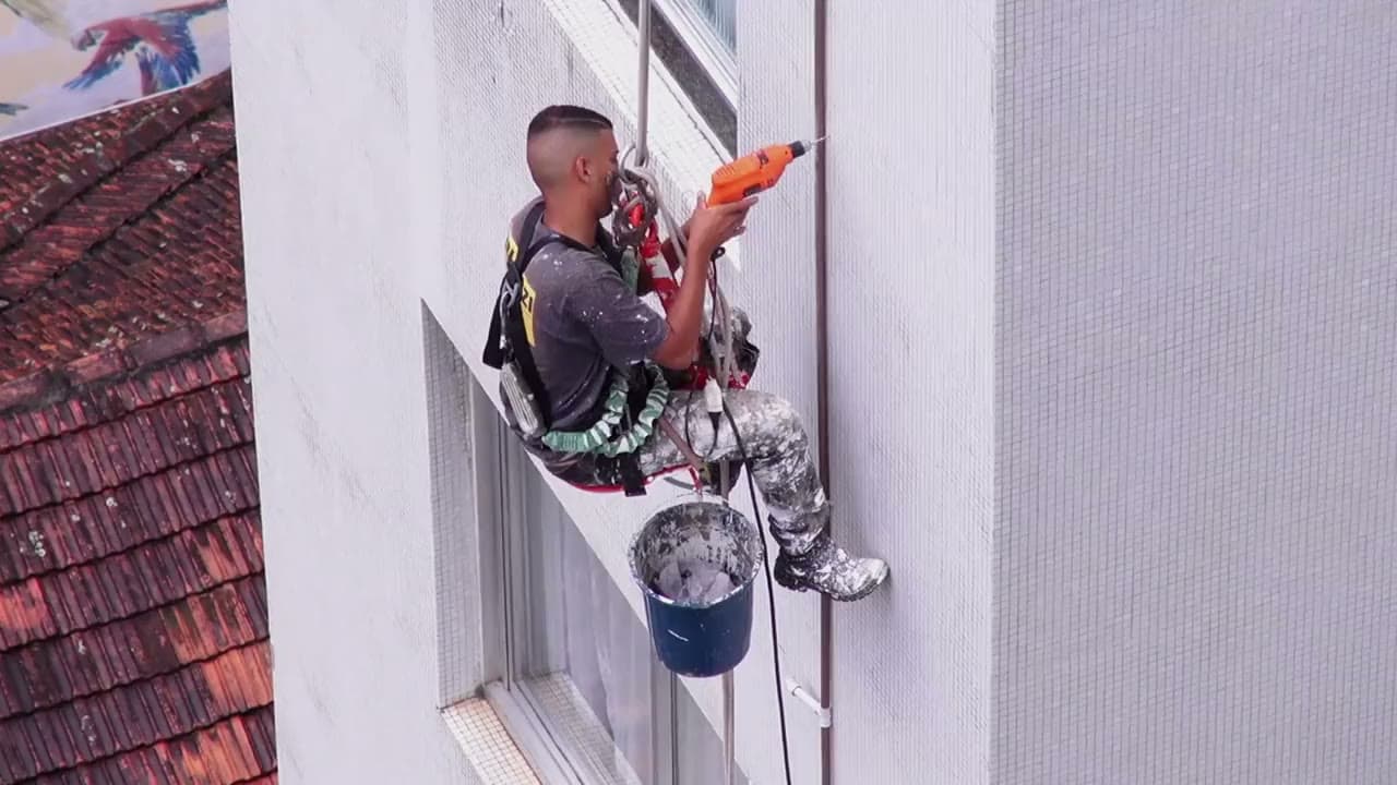 Un ouvrier travaille en hauteur sur une façade, suspendu dans un harnais de sécurité