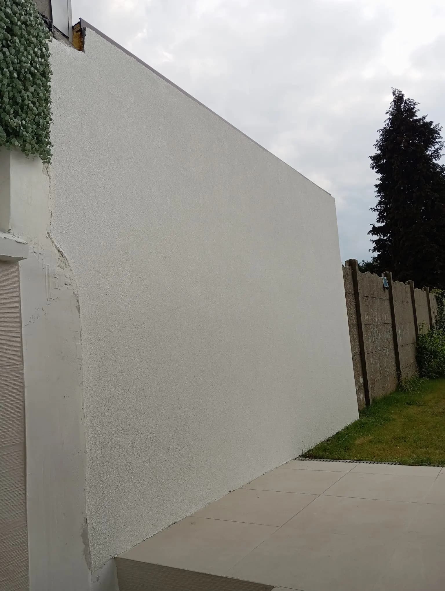 Mur d'annexe entièrement fini en crépi blanc, à côté d'une terrasse carrelée