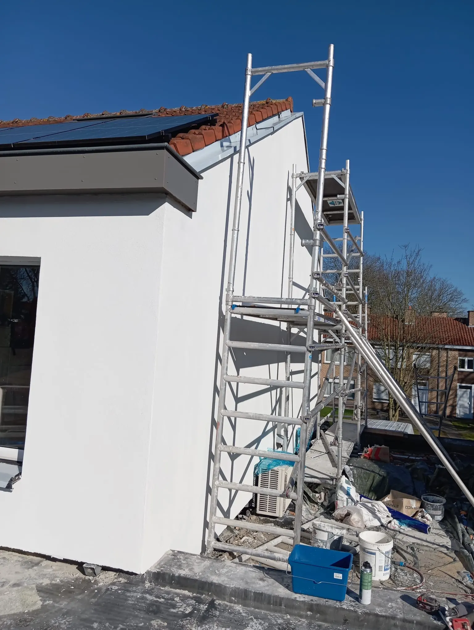 Pignon fini en blanc avec échafaudage roulant à côté et panneaux solaires sur le toit en tuiles