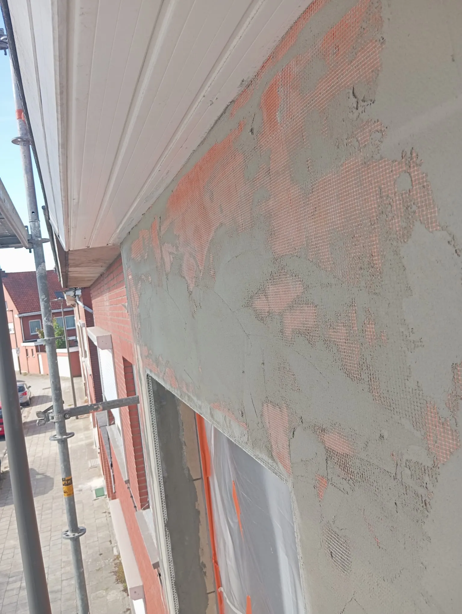 Façade à mi-chemin du processus d'enduit : mortier d'armature sur treillis orange, avec échafaudage