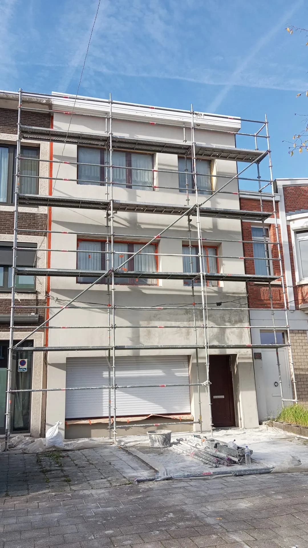 Façade complète de maison de rangée avec enduit frais, sous échafaudage et ciel bleu